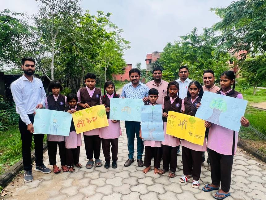 Students holding Ek Ped Maa Ke Naam posters on a tree lined campus path