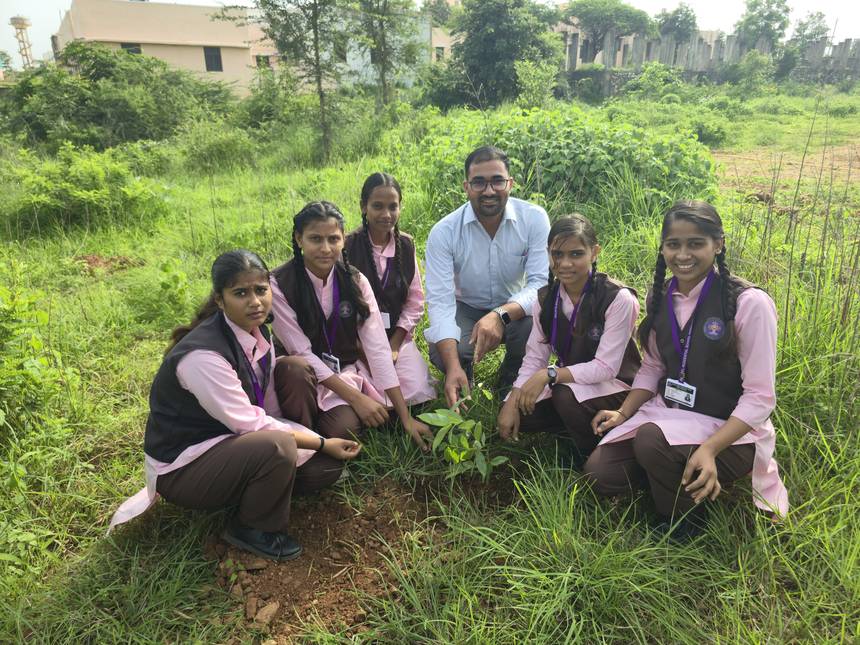 A teacher and students kneeling beside a newly planted sapling on the campus