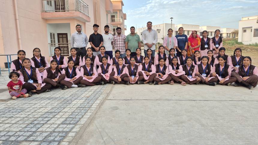 Students seated with teachers on the campus ground in front of the residential blocks