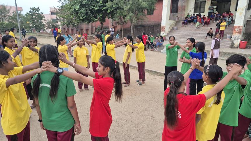 Students in coloured team shirts joining hands in a circle game on the playground
