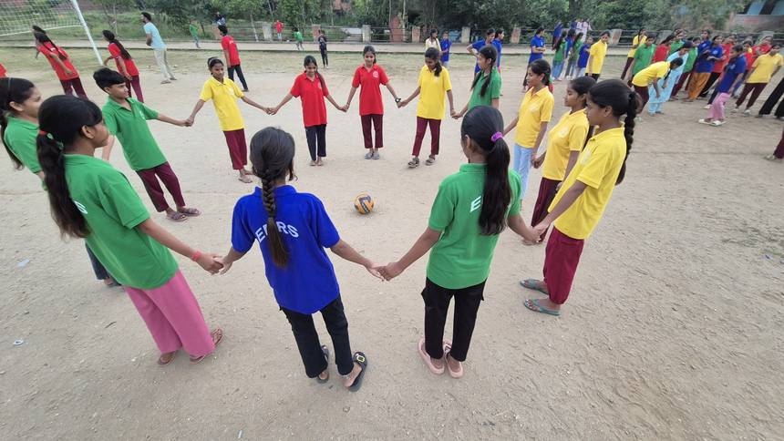 Students standing in a circle around a volleyball during a games period